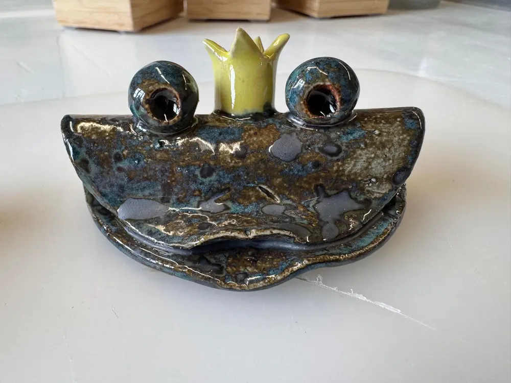 Handgefertigter Froschkönig aus Ton als Halter für einen gerollten Gutschein